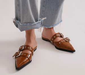 A stylish model showcases the SWIRL-01 Buckled Slip-On Flats by Beast Fashion in a brown hue, featuring dual buckle straps. These chic buckled slip-on flats are perfect for summer vacations and casual outings. Flat mules for a trendy summer look.